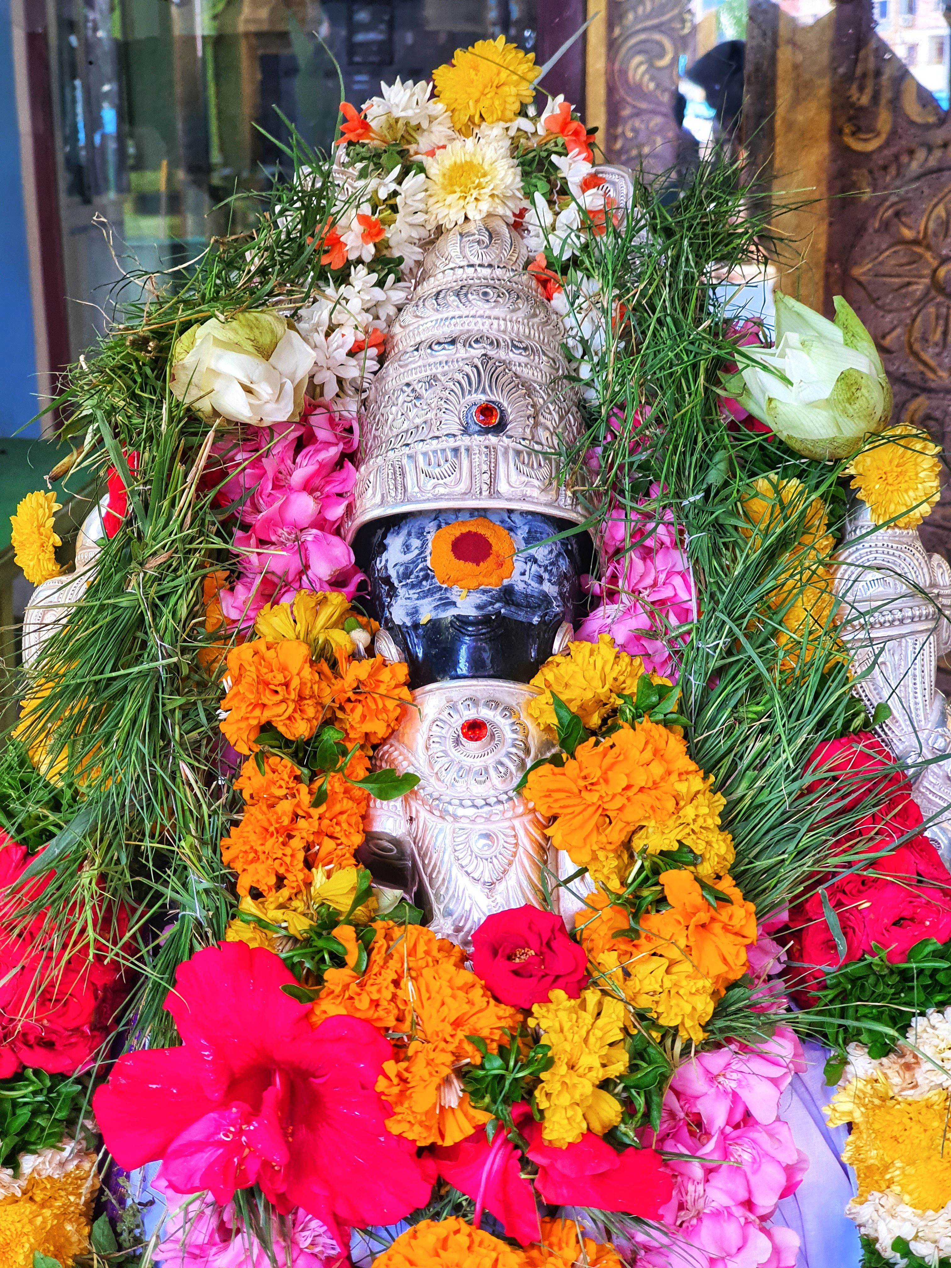Close-up of a Hindu deity statue decorated with colorful flowers and detailed ornaments, symbolizing spirituality.