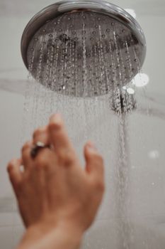A hand reaches toward a shower head, capturing water droplets in motion.