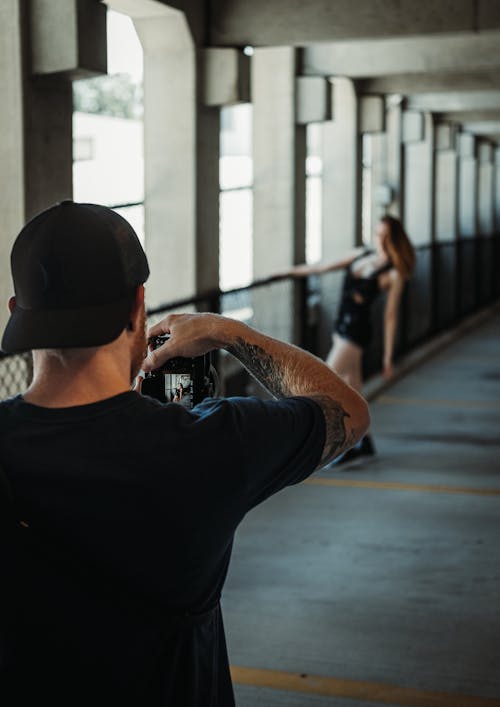 Man in Black Shirt and Black Cap Taking Photo of Woman in Black Mini Dress