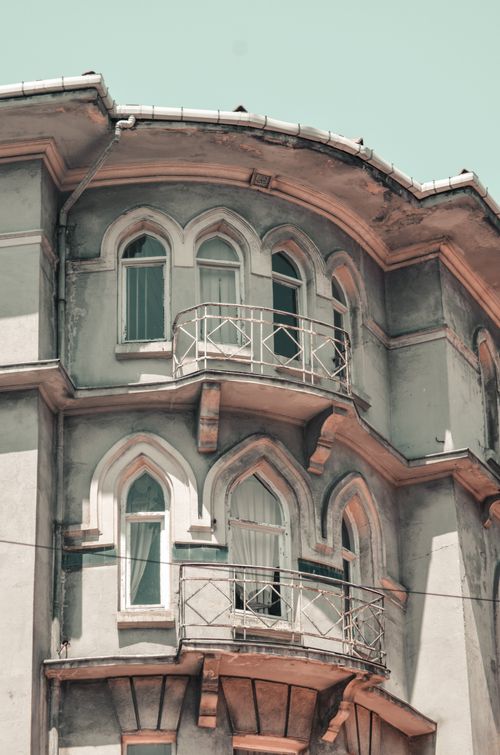Free Detailed view of a unique residential building exterior with arched windows and balconies under a pastel sky. Stock Photo