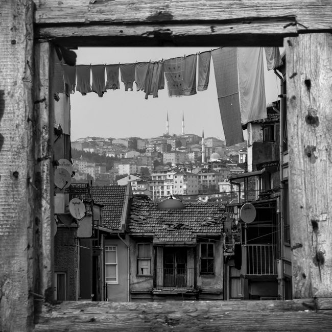 Black and white cityscape with clothes drying, viewed through a rustic window frame.