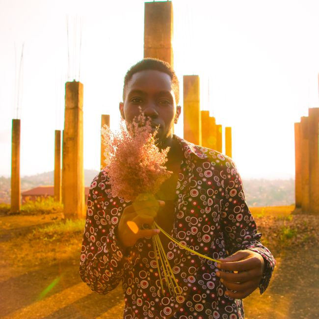 A portrait of a man holding flowers against a vibrant sunset in Kampala, Uganda.