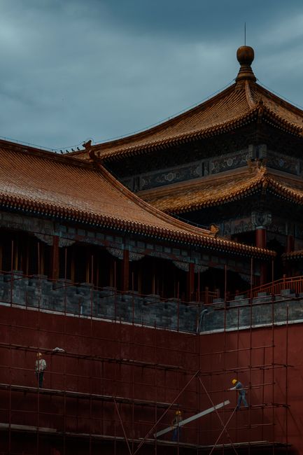Chinese pagoda with intricate roofs under renovation with workers on scaffolding.