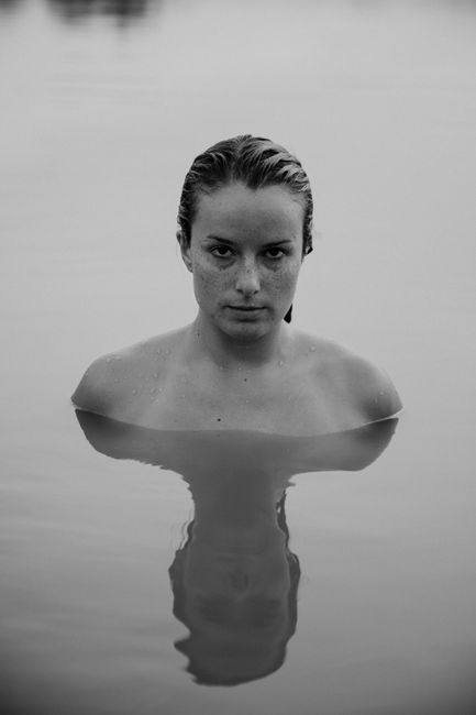 Black and white portrait of a woman submerged in calm water, exuding serenity.