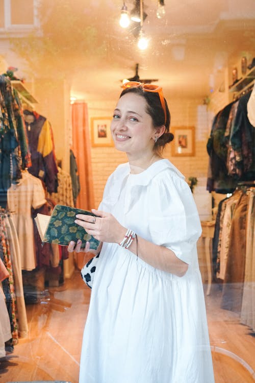 Woman Wearing a White Dress Holding a Notebook in a Fashion Store