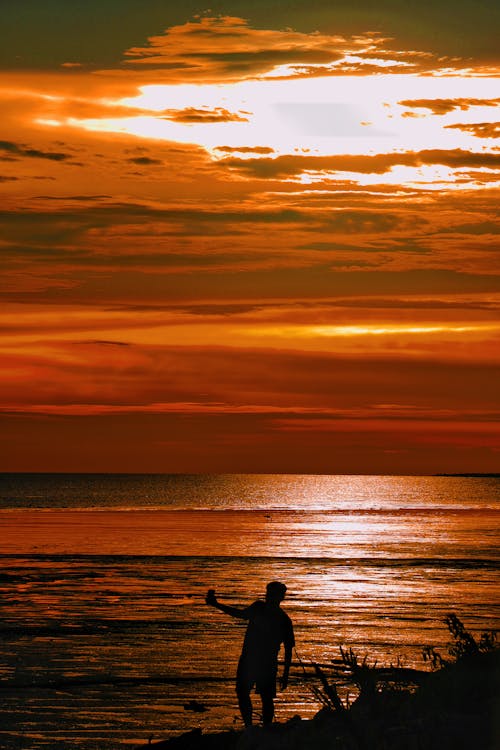 Silhouette of a Man Standing on a Seashore at Dramatic Sunset