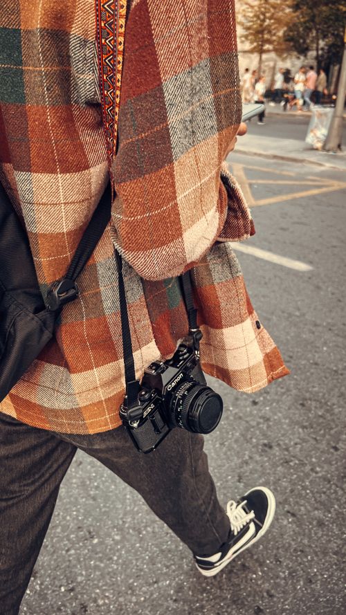 Free A person wearing a plaid coat walks on the city street, carrying vintage cameras. Stock Photo