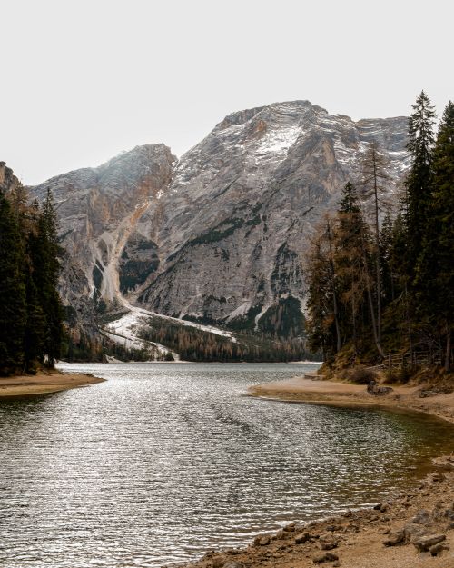 Free Discover the tranquil beauty of snow-capped mountains reflecting on a serene lake surrounded by pine trees. Stock Photo