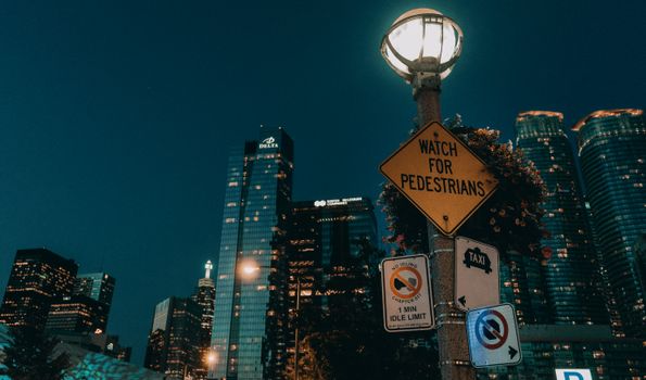 A vibrant nighttime cityscape of Toronto featuring illuminated skyscrapers and pedestrian signs.