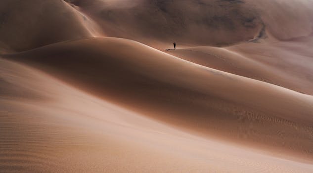 A lone person walks on vast sand dunes in Iran, embodying solitude and nature's beauty.