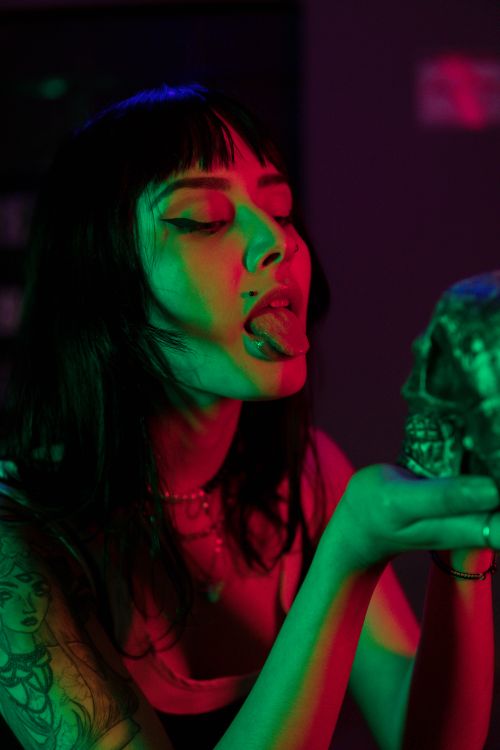 Free A woman poses with a skull under vibrant red and green neon lights, creating a surreal atmosphere. Stock Photo