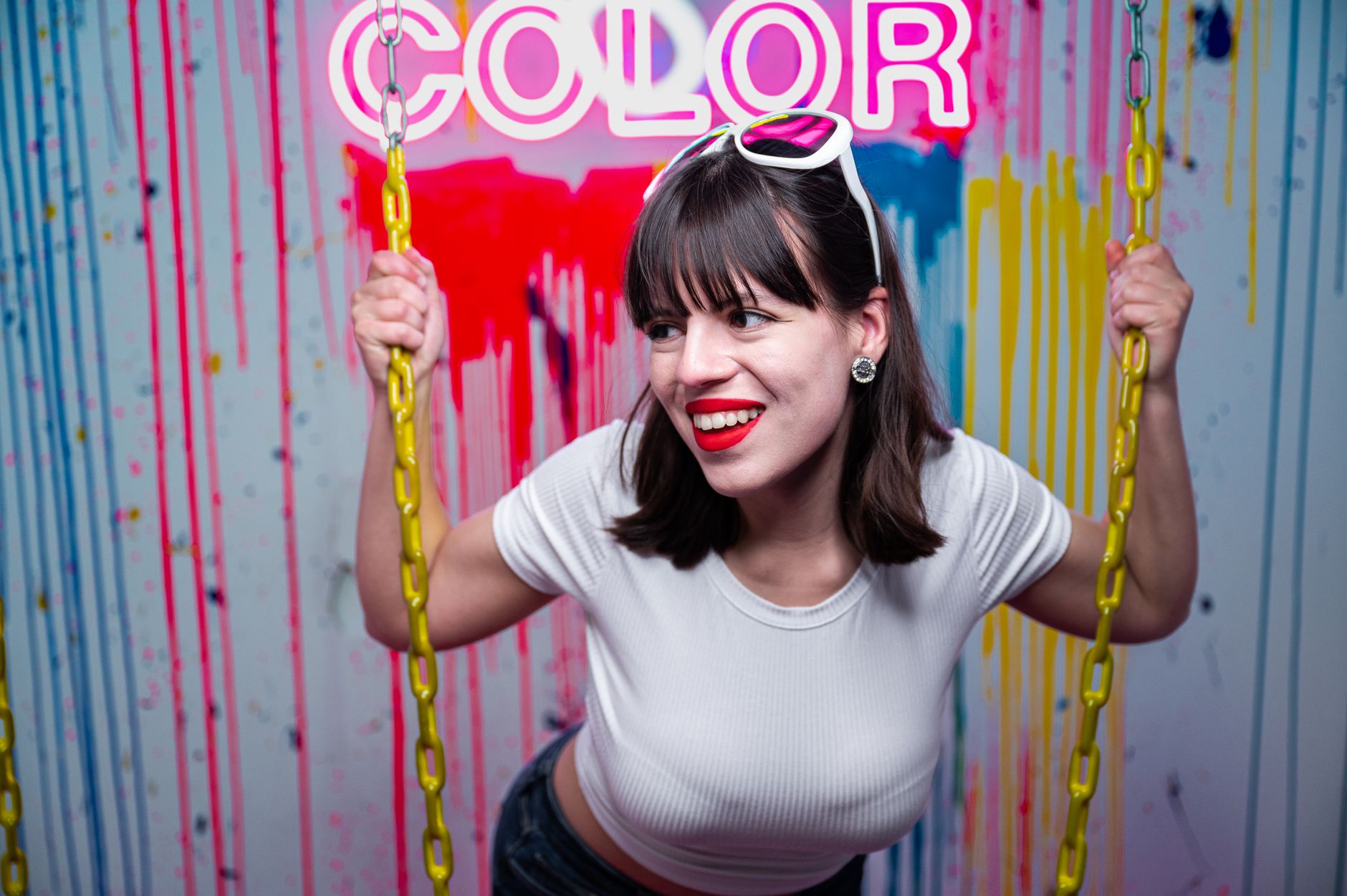 Young woman smiling on a swing with colorful neon lights and artistic background.