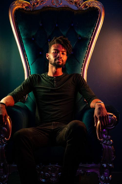 Free A man with a beard sits confidently in a regal chair, under moody lighting. Stock Photo