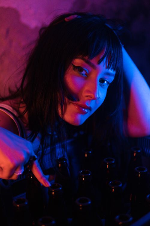 Free A vibrant portrait of a woman with bottles under colorful lighting. Stock Photo