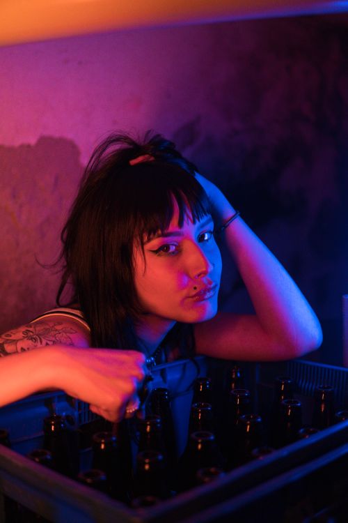 Free Tattooed woman poses with beer bottles in creative neon lighting, creating a modern artistic atmosphere. Stock Photo
