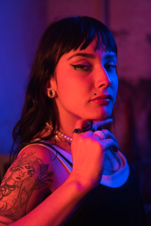 Free A vibrant, moody portrait of a woman with tattoos under colorful lighting. Stock Photo