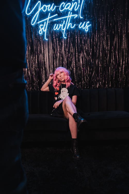 Woman in Black Outfit Sitting Under a Neon Signage