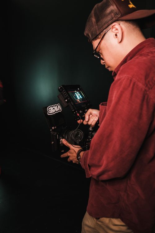 Free A focused photographer in a red shirt working with camera equipment indoors. Stock Photo