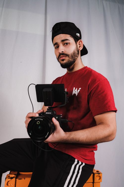 Free Young male videographer holding camera indoors, showcasing his professional equipment. Stock Photo