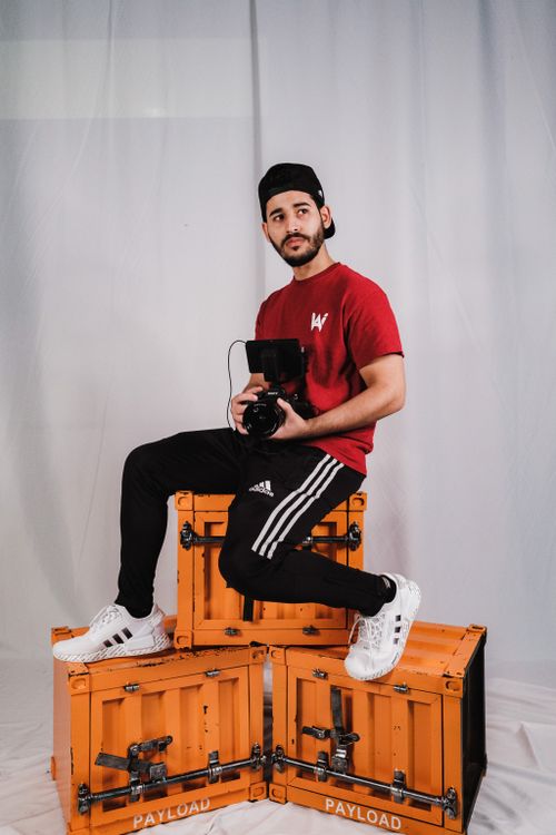 Free Man in red shirt holding camera sitting on orange boxes in studio. Stock Photo