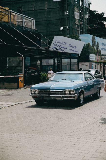 Vintage blue muscle car driving through a city street in daylight, capturing a retro vibe.