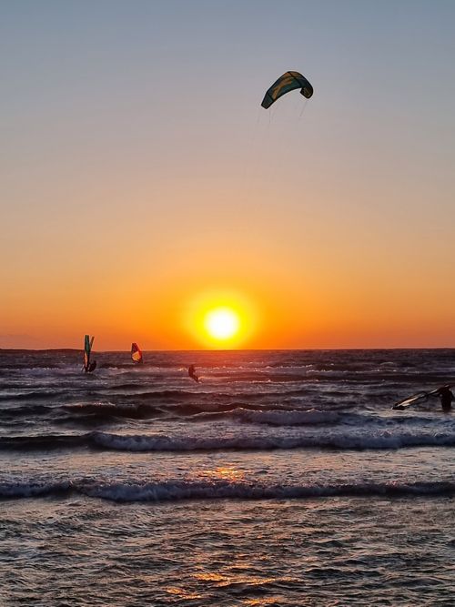 Free Kitesurfers catch waves against a vibrant sunset in Rhodes, Greece, capturing the thrill of water sports. Stock Photo
