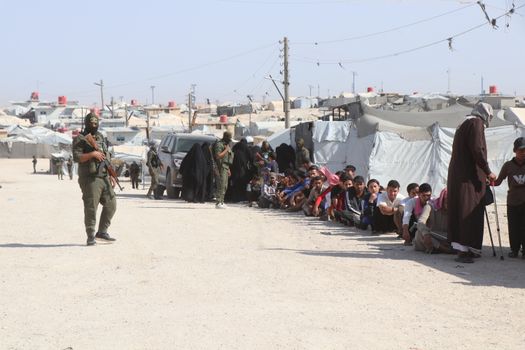 Refugees in al-Hol camp, Syria, guarded by soldiers, highlighting humanitarian crisis.