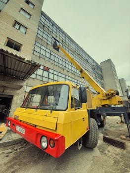 Yellow crane truck parked near a factory building in Derhachi, Ukraine.