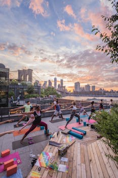 Group of people practicing yoga outdoors with NYC skyline and sunset view.