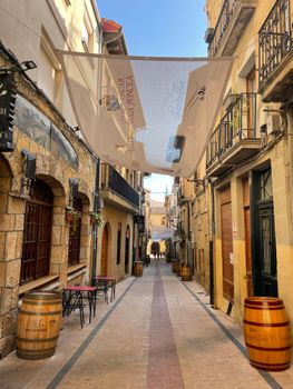 Picturesque narrow alley in a historic European town with stone buildings and wooden barrels.