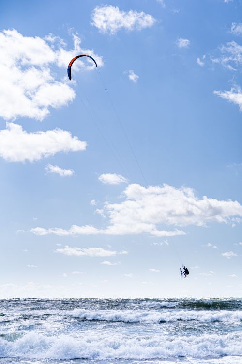 Free Dynamic kite surfing over ocean waves against a clear blue sky. Perfect for water sports enthusiasts. Stock Photo