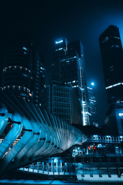 Free Dynamic urban skyline featuring illuminated skyscrapers with a futuristic walkway at night. Stock Photo