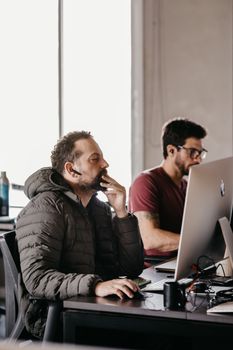 Two male office workers concentrating on their desktop computers in a modern workspace.