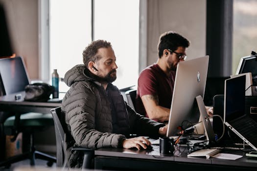 Two men collaborating in a modern office setting, focused on computers.