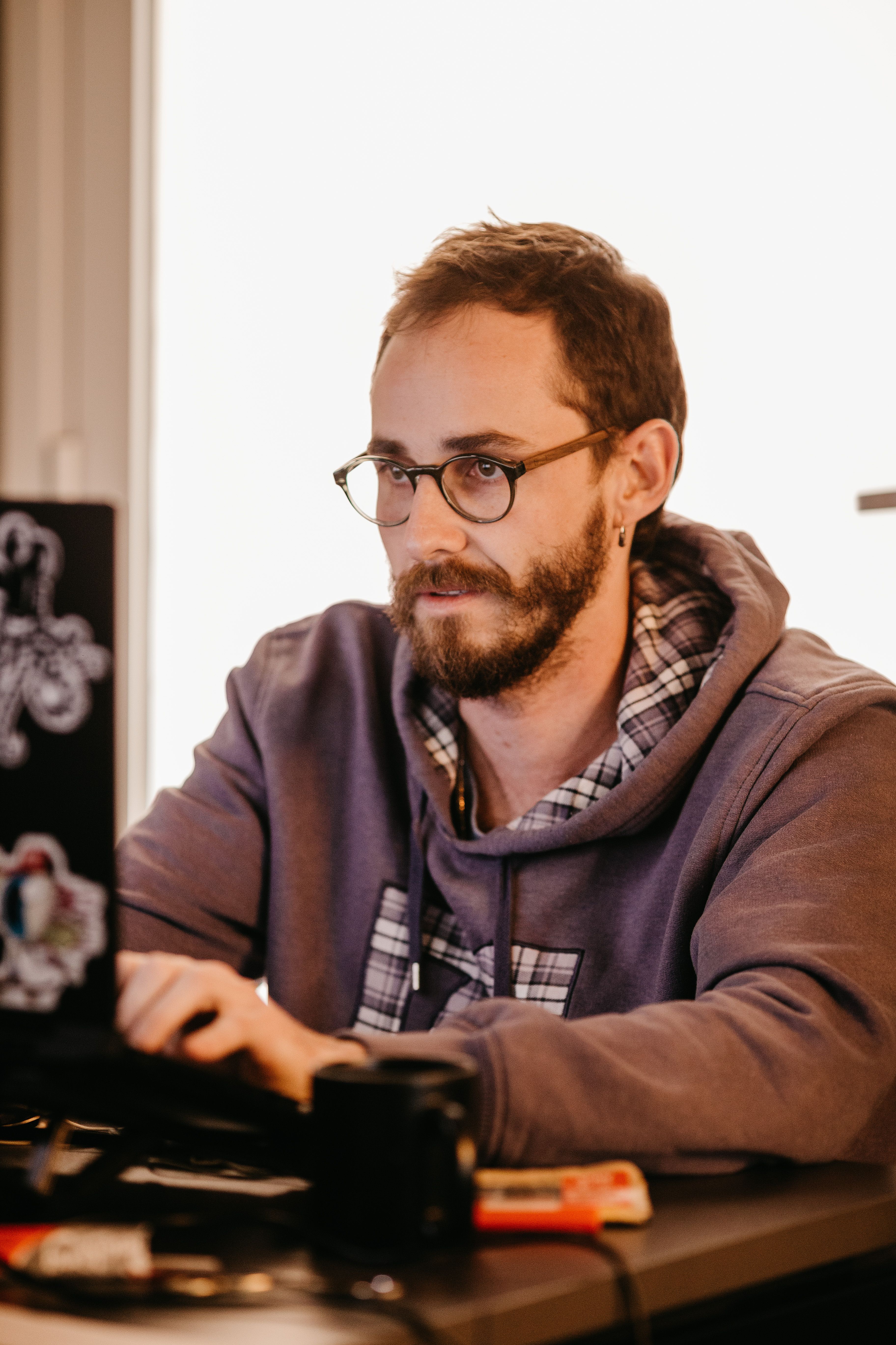 An adult man with glasses and beard works intently on a laptop in a cozy indoor setting.
