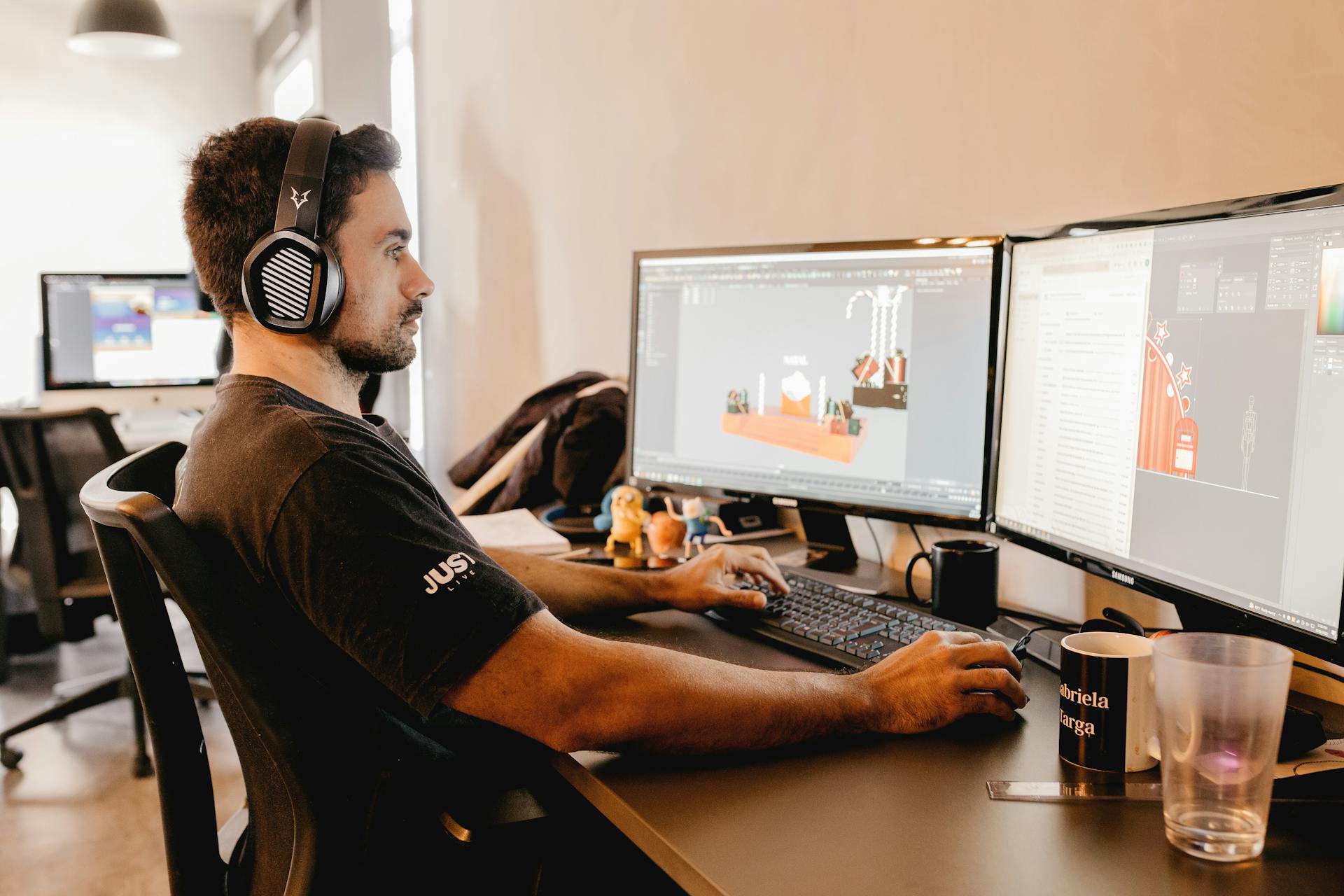 A man wearing headphones works on a computer with two monitors in a modern office setup.