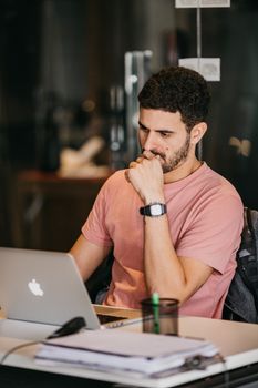 Thoughtful man in a casual office setting working on a laptop, focusing intensely.