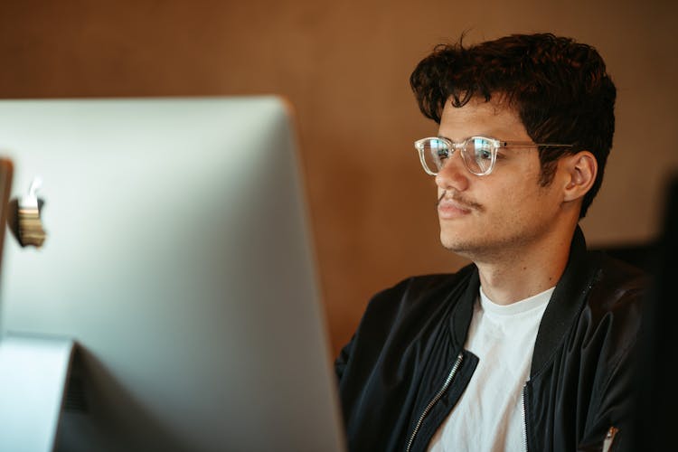 A Man Wearing Eyeglasses Looking At The Screen Of A Computer