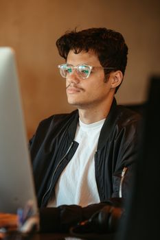 Focused young man in glasses working at a computer in a cozy office environment.