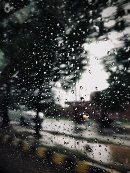 Raindrops on glass with a blurred outdoor view, capturing a moody rainy scene.