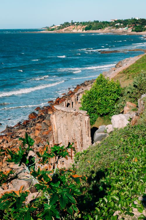 Free A beautiful coastal scene featuring a rocky shoreline and lush greenery under a clear blue sky, perfect for summer impressions. Stock Photo