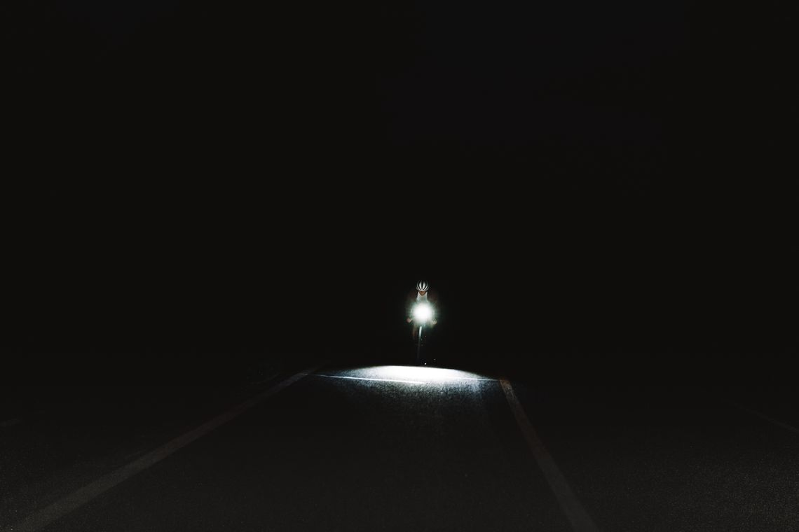 Cyclist riding on a dark road at night illuminated by bicycle lights
