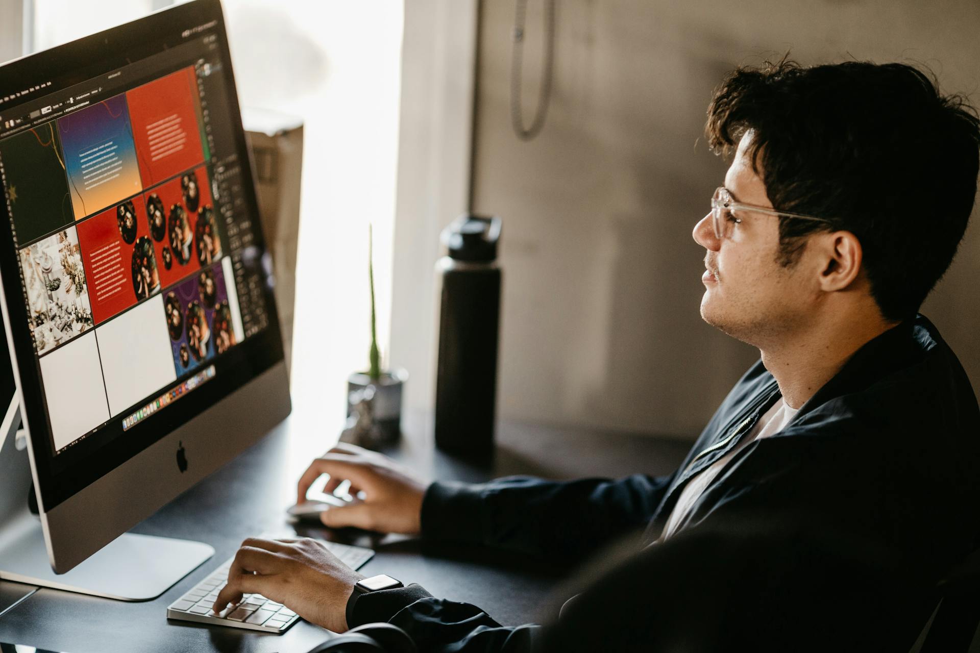 A focused graphic designer working on a computer in a modern office setting with creative visuals on the screen.