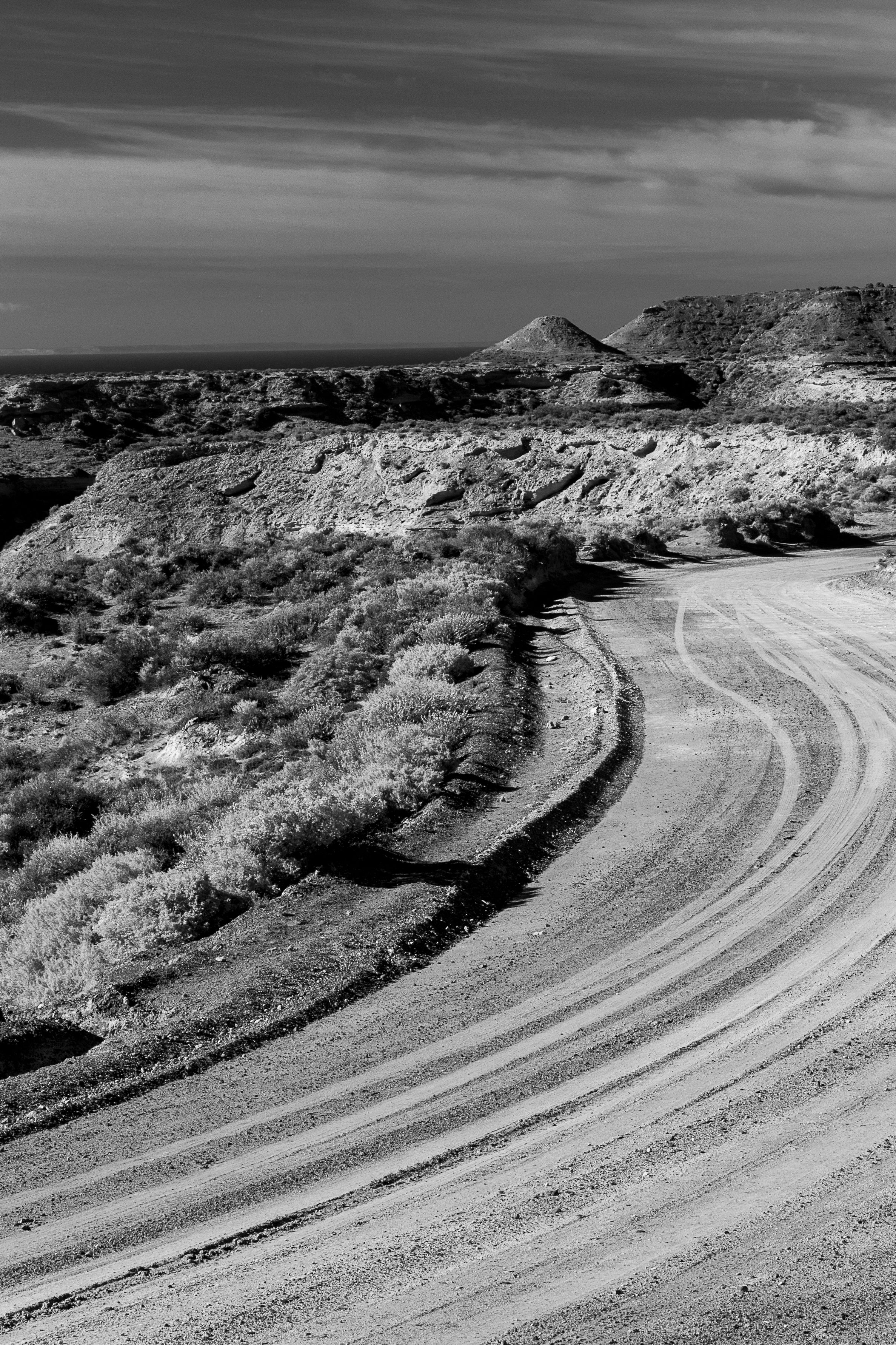 Captivating black and white shot of a winding road through a rugged desert landscape under a dramatic sky.
