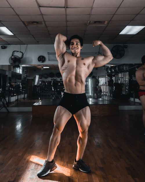 Free Shirtless bodybuilder flexing muscles in a well-lit gym, showcasing strength and fitness. Stock Photo