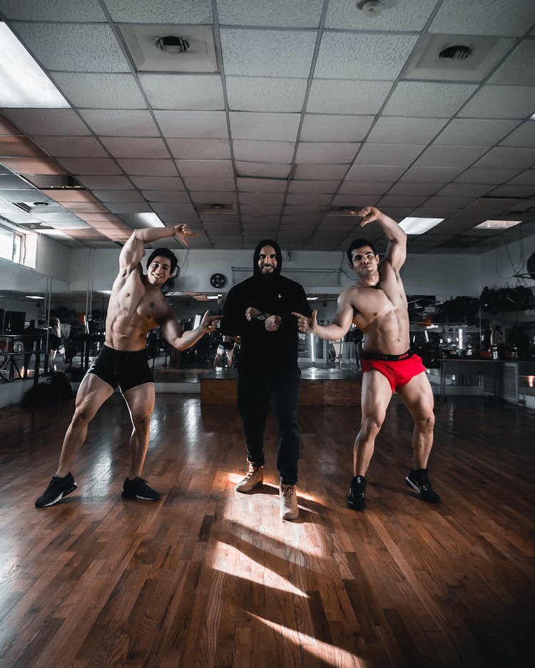 Shirtless Men Flexing Muscles And Standing Inside A Gym