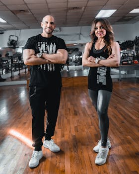 Confident couple in active wear posing with arms crossed in a gym setting.