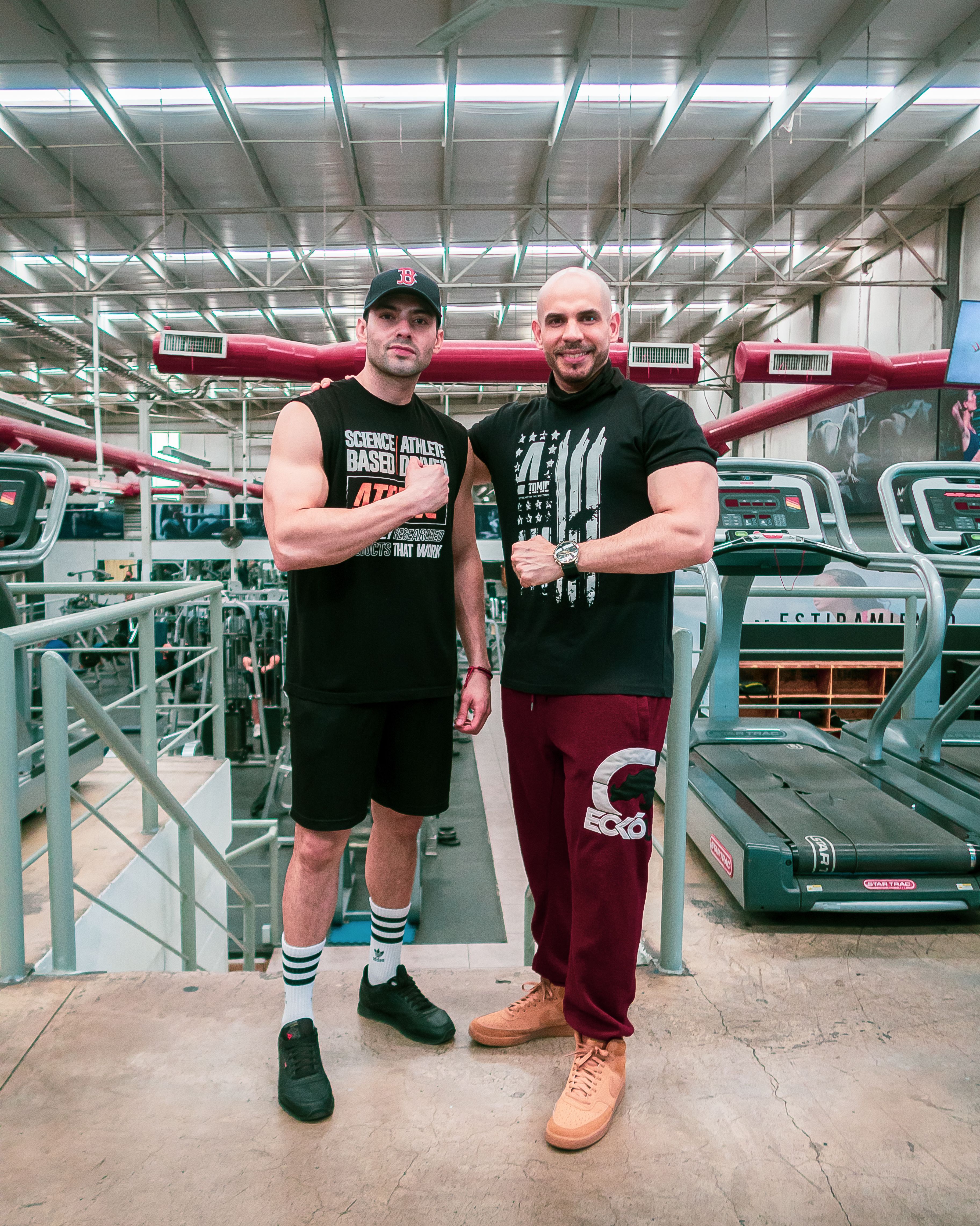 Two muscular men posing confidently in a modern gym, highlighting fitness and camaraderie.