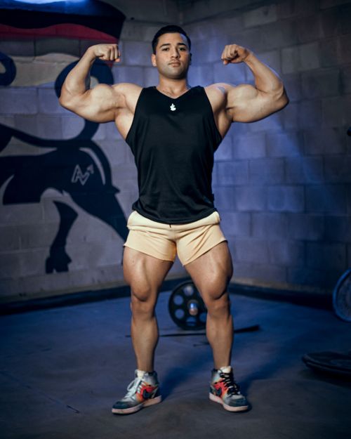 Free A muscular man in a black tank top flexes in an indoor gym setting, showcasing strength and fitness. Stock Photo