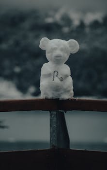 A charming snow bear sculpture perched on a fence embraces the winter scenery.